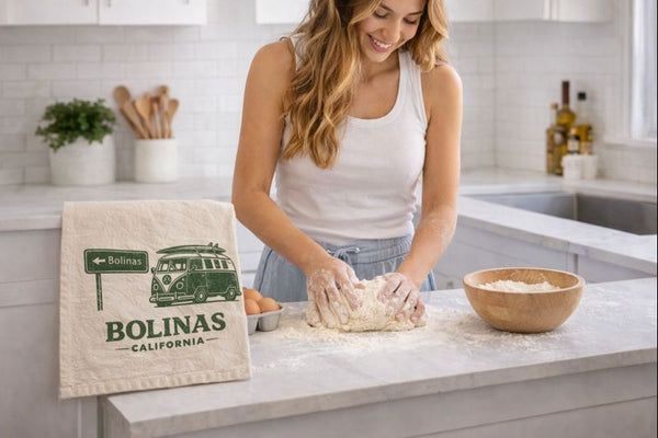 Woman kneading dough in a kitchen with a 'Bolinas, California' tote bag on the counter.