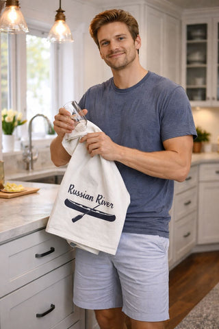 Man holding a organic tea towel with 'Russian River' text in a kitchen.