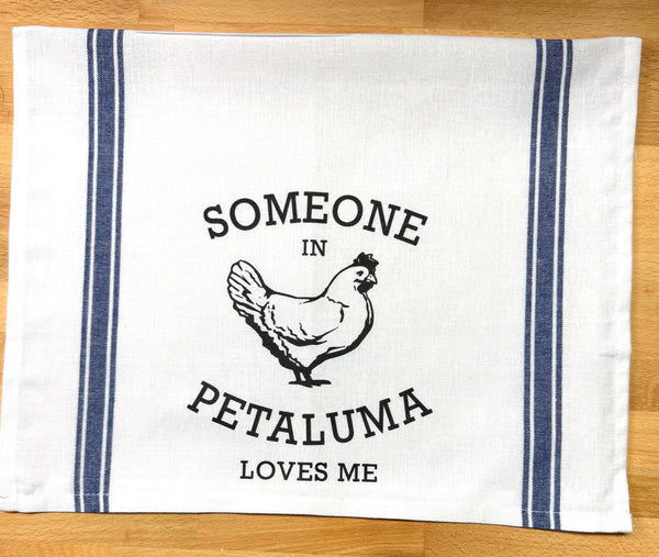 White towel with  blue stripe with a chicken and a saying "Someone in Petaluma Loves Me"