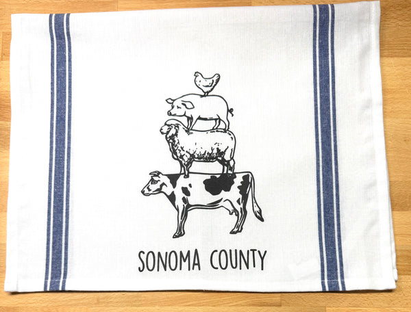 Tea towel with farm animal illustration and 'Sonoma County' text on a wooden surface