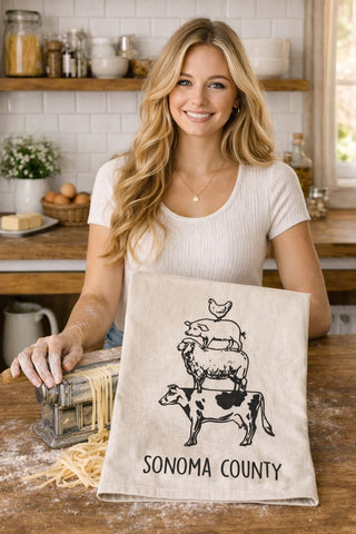 Woman holding a towel with 'Sonoma County' animal stack design in a kitchen setting